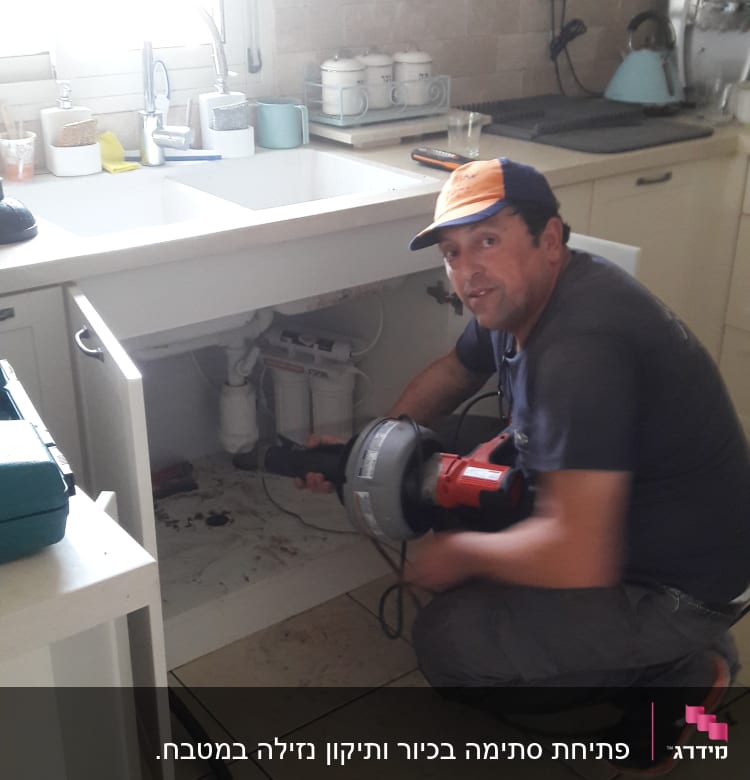 אינסטלטור עובד מתחת לכיור עם כלי עבודה חשמלי